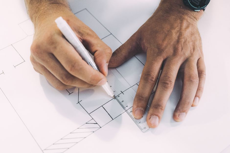Close-up of an architect's hands carefully drawing complex modern blueprints, representing the strategic planning required to build a new GEO retainer service.