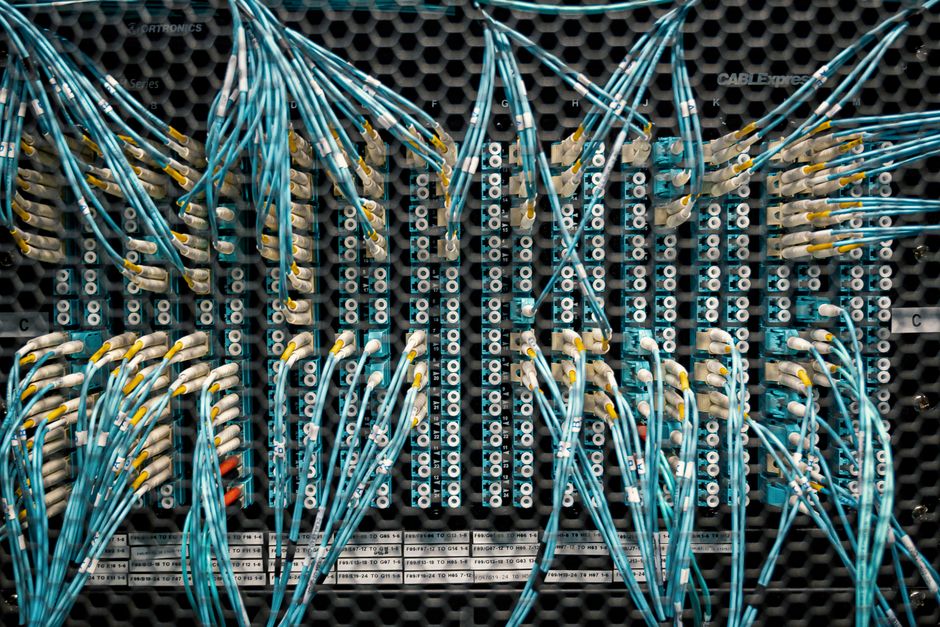 Close-up of glowing blue fiber optic cables inside a modern server rack, representing the high-speed infrastructure of pus...