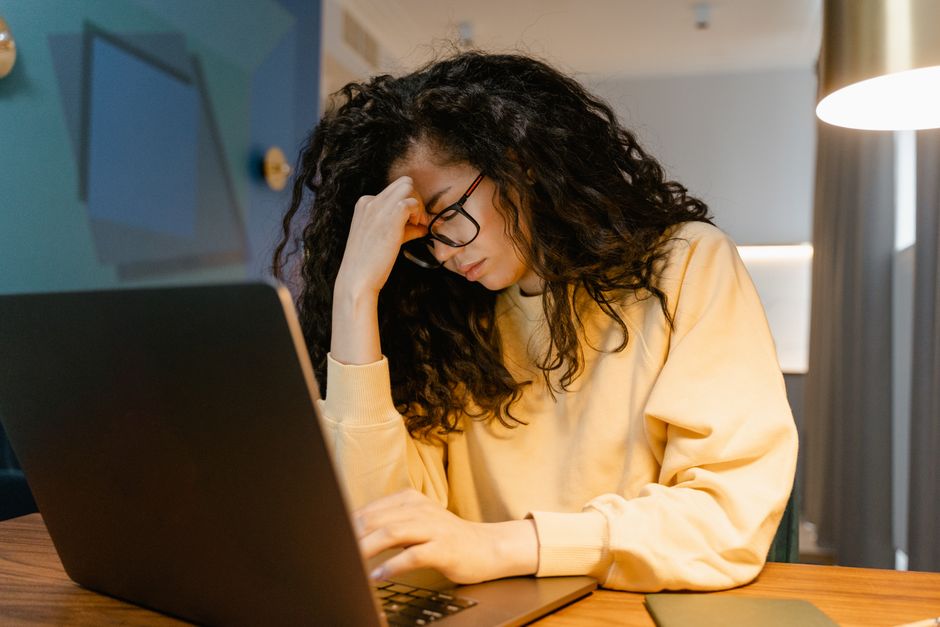 A person sits at their desk in a dimly lit office, looking stressed and frustrated at their computer, representing the profitability drain from bad tools.