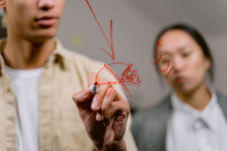 A person's hand uses a marker to draw a clear strategic diagram on a modern glass wall, representing a new framework and blueprint for success.